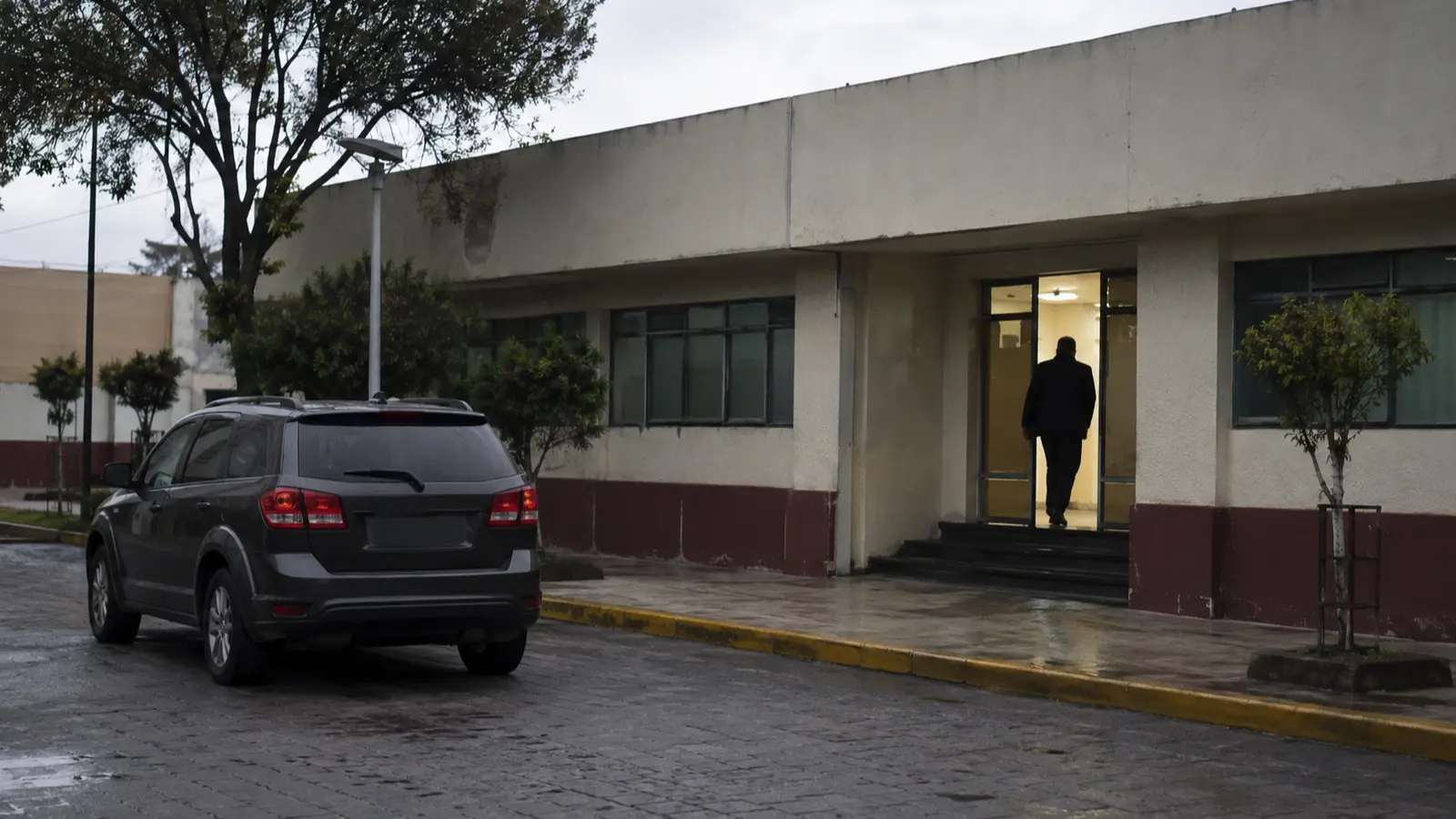 Silueta anónima entra a un edificio municipal junto a un vehículo sin insignias