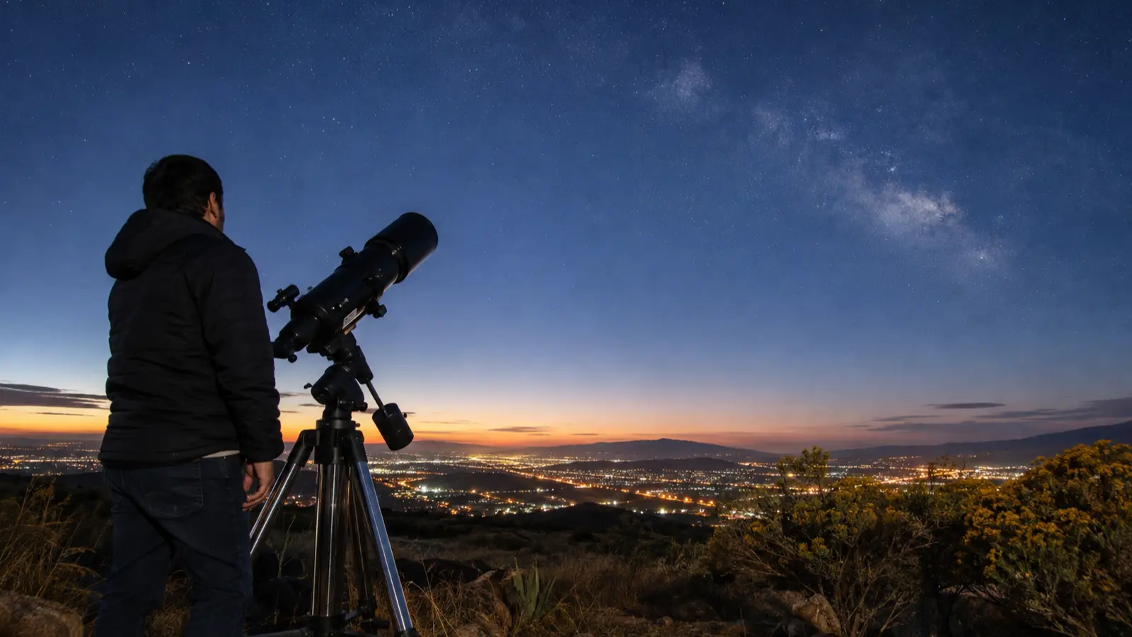 Persona observa el cielo nocturno con un telescopio desde una colina de Puebla