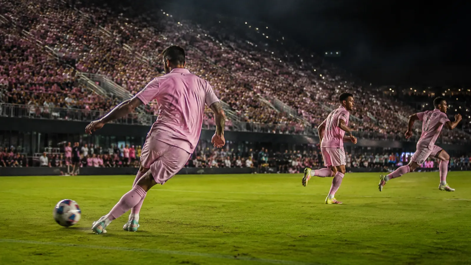 Futbolista con uniforme rosa prepara un pase durante un partido nocturno
